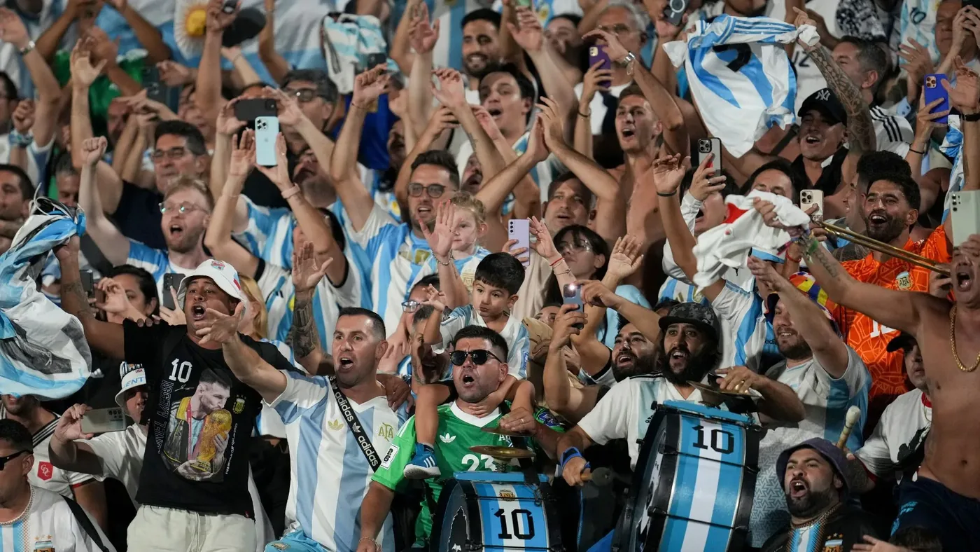 Tres ciclistas argentinos con mochilas y bicicletas cruzando una carretera durante su viaje hacia la Copa Mundial 2026